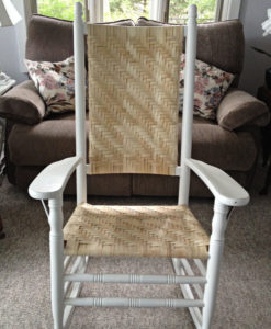 White wicker rocking chair with woven herringbone pattern, sitting in a living room